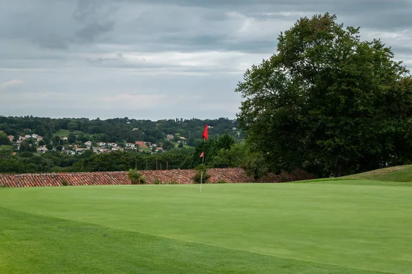 Grassed golf course with a red flag on the green grass on a very cloudy day
