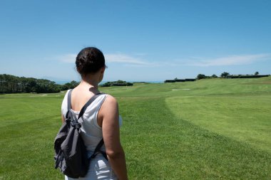 Güneşli bir günde, arka planda deniz olan güzel manzaranın tadını çıkaran golf sahasındaki kadın.
