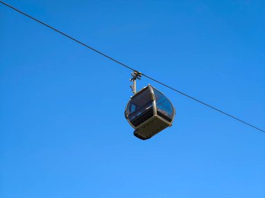 Çelik kabloda mavi gökyüzü olan teleferik kabini. Kablolu TV ile gezmekten ve manzaradan hoşlanan insanları taşıyorlar.