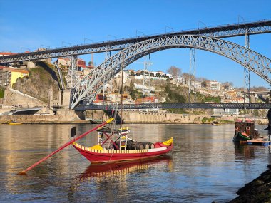 Rabelo boat over the Douro river in Ribeira in Vila Nova de Gaia, with the historic metal bridge Dom Luis I and part of the old city in the background clipart