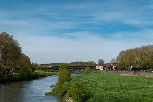 Fransa 'nın Bask Bölgesi' ndeki Dax şehrinde hızlı bir trenin geçtiği arka planda bir köprüyle Adour nehri üzerindeki panoramik manzara