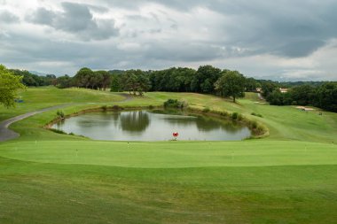 Yeşil golf sahaları ve çok bulutlu bir gökyüzünün altında bir göl arasında