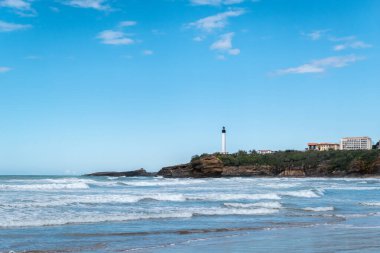 Küçük dalgalı sahil, büyük bir kaya oluşumunun üzerindeki uzak deniz feneri Biarritz 'in sahil güzelliği.