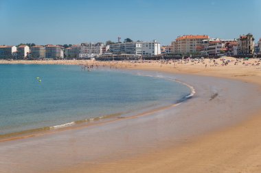 Saint Jean de Luz Plajı 'nda güneşli bir gün. Sahilde yüzenler ve şehirde turistler var.