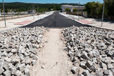 Yeni asfalt döşemeli, restorasyonlu bir yolu olan inşaat sahasında, bir köyün ortasında küçük granit küplerden oluşan paralel zeminlerin devamı var.