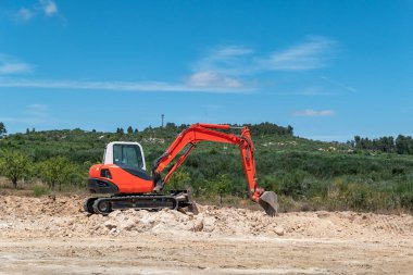 Sürüngen kepçesi mavi gökyüzünün altında ve doğanın ortasında kayalık arazide çalışıyor.