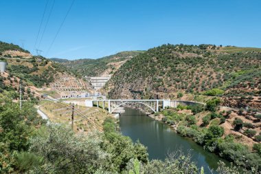 Portekiz 'in Tras-os-Montes kentinin arka planında Foz Tua hidroelektrik barajı bulunan tepeler ve dağlar arasındaki Tua Nehri üzerindeki köprü.