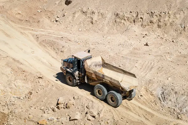 stock image Dump truck driving in arid and rugged terrain for earthmoving