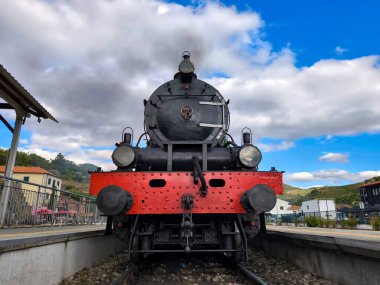 Demiryolu istasyonunda klasik buhar lokomotifi. Güneşli bir günün ortasında şöminede yanan kömürden siyah bir duman çıkıyor.