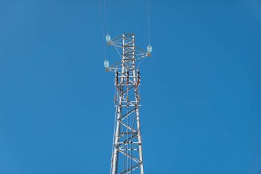 Mavi gökyüzüne karşı yüksek voltajlı elektrik hatlarıyla elektrik direği