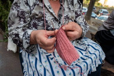 Huzurlu bir ortamda bir bankta otururken örgü iğneleriyle yün ören bir insan.