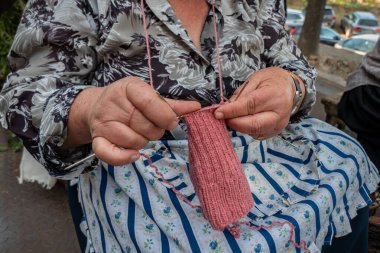 Bir bankta oturan kadın, sakin bir şekilde örgü iğneleriyle yün örüyor, açık hava ortamında.