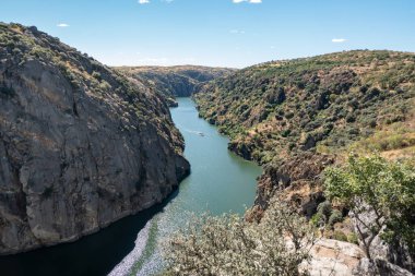 Dağlarla, bitki örtüsüyle ve mavi gökyüzüyle doğal bir manzaranın ortasında Portekiz 'in arka planında küçük bir tekne olan Miranda do Douro Nehri.
