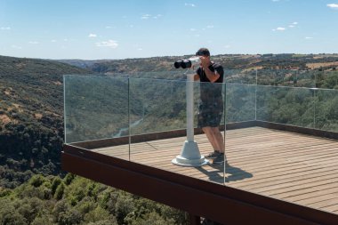 Miranda do Douro 'daki Penha das Torres' in genç turisti Portekiz 'in arka planındaki güzel manzarayı gözlemlemek için dürbün kullanıyor.