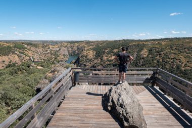Penha das Torres 'in Miranda do Douro' daki kayanın tepesindeki genç turist Portekiz 'in arka planındaki manzarayı inceliyor.