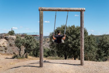 Portekiz 'de Miranda do Douro' da Penha das Torres bakış açısı yakınında salıncakta sallanan genç bir turist.