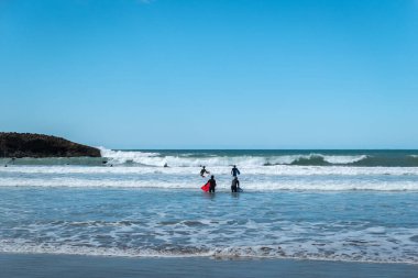 Bazı sörfçüler mavi gökyüzüne karşı dalgaların tadını çıkarırlar.