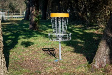 In search of the basket. The thrill of disc golf in the middle of nature among trees and shadows clipart