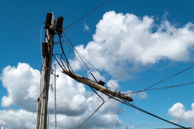 Bozuk telefon ve fiber optik direk. Mavi bir gökyüzünün altında asılı duran kablolar ve bulutlar.