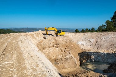 Mavi gökyüzü altında tarım amaçlı bir su barajı inşa edilirken kazıcı faaliyet gösteriyor