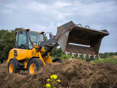 Bulutlu bir günde yol yapımı için tarımsal bir çiftliğin ortasına toprak yaymaya çalışan bir tekerlek yükleyici.