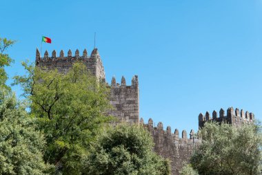 Bitkilerin arasında, Portekiz ulusunun beşiğinin ortaçağ duvarları, mavi gökyüzünün altındaki Guimaraes Kalesi 'nin dışı.