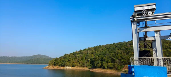 Açık mavi gökyüzü ve yeşil orman arka planına sahip bir nehir, hidroelektrik santrali olan yaz manzarası