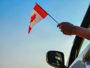 Boy waving Canada flag against the blue sky from the car window close-up shot. Man hand holding Canadian flag, Copy space