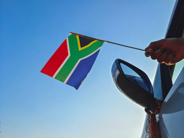Boy waving South Africa flag against the blue sky from the car window close-up shot. Man hand holding South African flag, Copy space