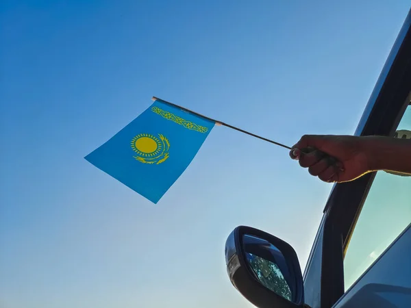 Boy waving Kazakhstan flag against the blue sky from the car window close-up shot. Man hand holding flag of Kazakhstan, Copy space