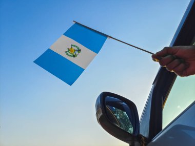 Boy waving Guatemala flag against the blue sky from the car window close-up shot. Man hand holding Guatemalan flag, Copy space 