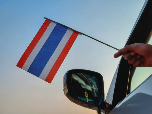 Boy waving Thailand flag against the blue sky from the car window close-up shot. Man hand holding Thai flag, Copy space