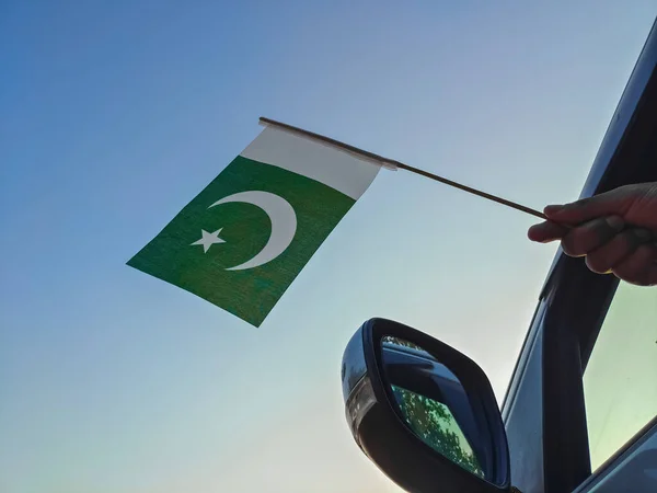 Boy waving Pakistan flag against the blue sky from the car window close-up shot. Man hand holding Pakistani flag, Copy space