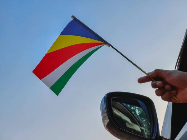 Boy waving Seychelles flag against the blue sky from the car window close-up shot. Man hand holding flag of Seychelles, Copy space 