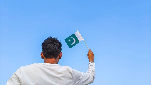 Boy holding Pakistan flag against clear blue sky. Man hand waving Pakistani flag view from back, copy space for text