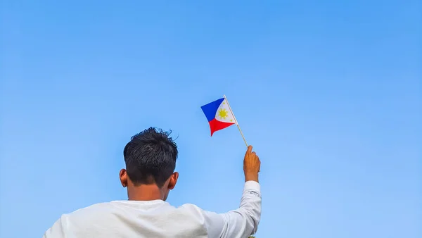 Boy holding Philippines flag against clear blue sky. Man hand waving Filipino flag view from back, copy space for text