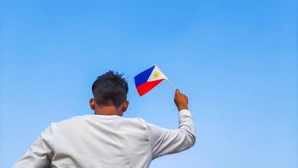 Boy holding Philippines flag against clear blue sky. Man hand waving Filipino flag view from back, copy space for text
