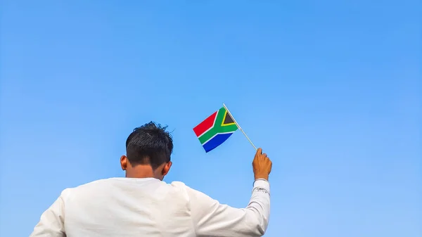 Boy holding South Africa flag against clear blue sky. Man hand waving South African flag view from back, copy space for text
