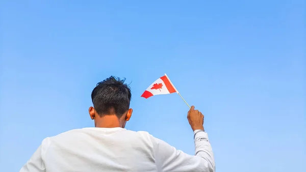 stock image Boy holding Canada flag against clear blue sky. Man hand waving Canadian flag view from back, copy space for text