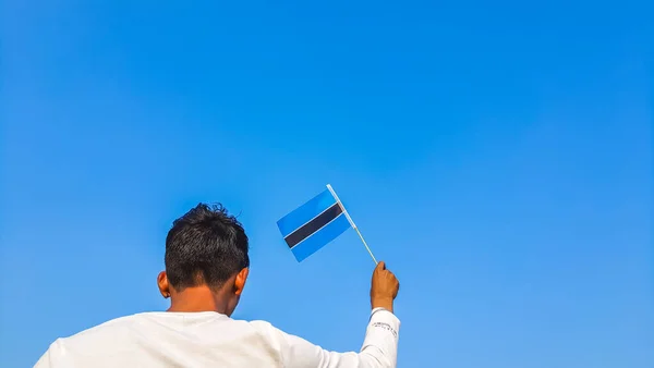 Boy holding Botswana flag against clear blue sky. Man hand waving flag of Botswana view from back, copy space for text