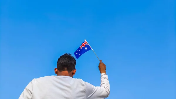 Boy holding Australia flag against clear blue sky. Man hand waving Australian flag view from back, copy space for text
