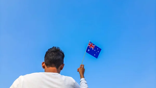 stock image Boy holding Australia flag against clear blue sky. Man hand waving Australian flag view from back, copy space for text