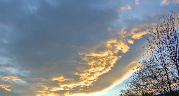 Farklı tonlarda ve renklerde bulutlar, güneş tarafından parlak bir şekilde aydınlatılır, gökyüzünü doldurur..