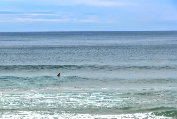 Genç adam sörf tahtasına sabırla oturmuş mükemmel dalgayı bekliyordu..
