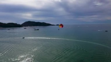 Phuket 'te parasailing. Güneşli bir sahilde, renkli bir paraşüt kanadı ya da paraşütle uçan bir adamın küçük bir görüntüsü.