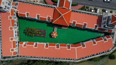 Yukarıdan yeşil renk ve otelin içindeki açık deniz yüzme havuzunun muhteşem kırmızı çatısı görünüyor..