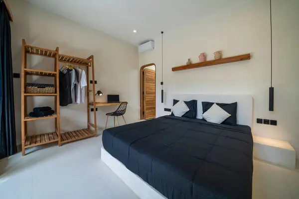 Simple design, ad, offer and modern home style. Double bed with pillows, soft blanket, carpet, lamp, armchair and furniture, on wooden floor. White wall, big window with curtains in bedroom interior.