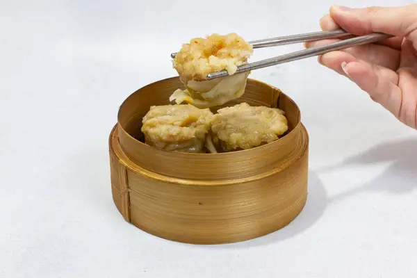 Buharda pişmiş shumai ya da Çin Dimsum 'unu geleneksel bambu budan çıkarmak için çubuk kullanan bir elin yakın çekimi..