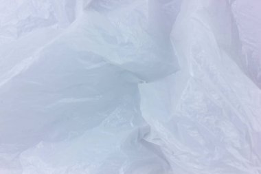 Kırışık beyaz bir plastik yaprağın soyut dokusu yumuşak ve şeffaf bir yüzey oluşturuyor. Buruşmuş madde ilginç ışık ve gölge desenleri oluşturuyor..