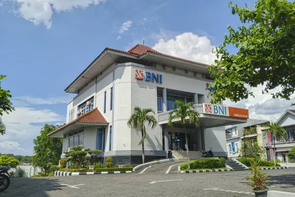 Surakarta - Endonezya, 18 Mayıs 2025: Bank BNI (Bank Negara Endonezya) binasının görüntüsü, parçalı bulutlu mavi gökyüzü altında. Beyaz binada kırmızı kiremitli çatılar ve belirgin 
